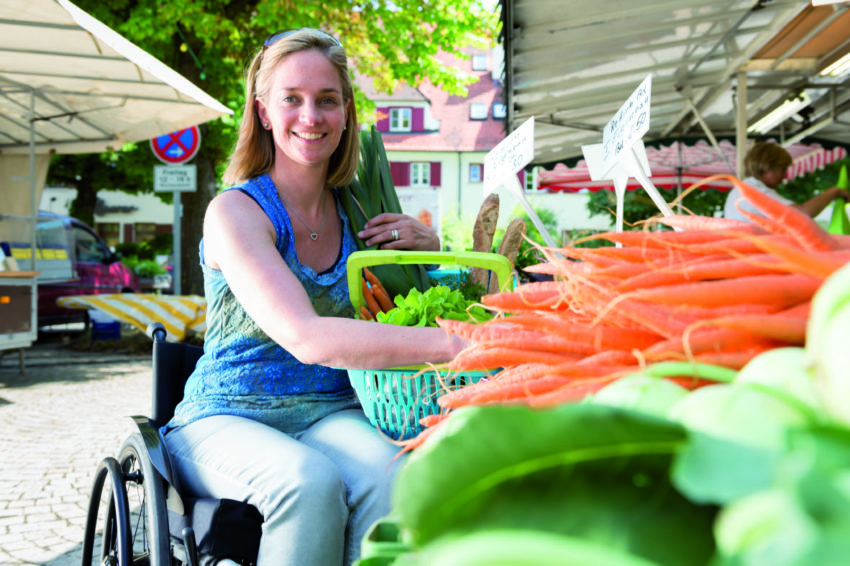 Fokus på sundhed - Ung, kvindelig kørestolsbruger handler ind på udendørs marked. Sund kost!